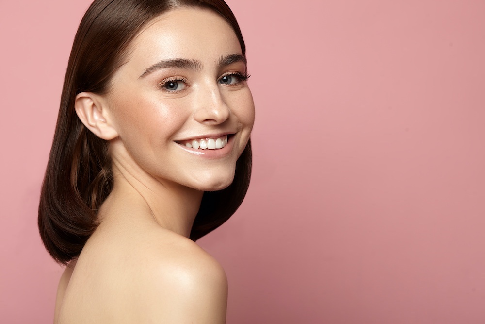 Beautiful smiling woman with clean skin, natural makeup and white teeth on a pink background